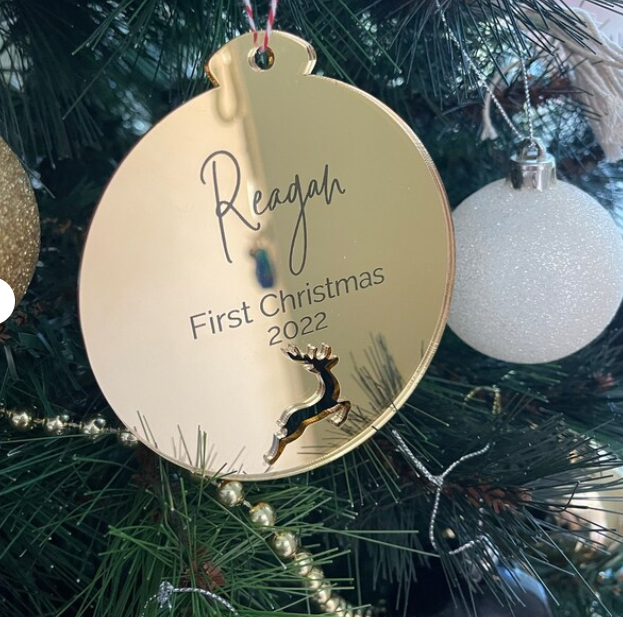 Gold Christmas ornament with 'Reagan First Christmas 2022' on a tree.