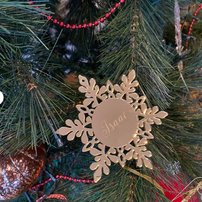 Decorative gold snowflake ornament with 'Isaac' engraved on a Christmas tree.