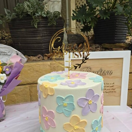 Decorative cake with floral designs on a table with plants and a framed picture in the background - Coast and Sun Creations