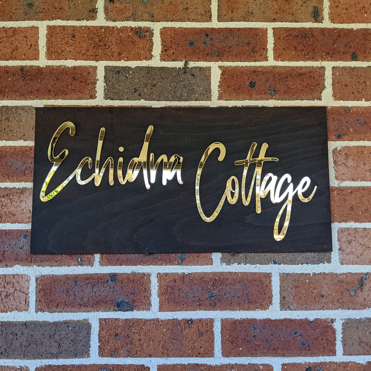 Gold Echidna Cottage welcome sign on a brick wall