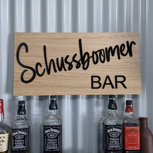 Wooden sign with 'Schussboomer Bar' text above liquor bottles on a corrugated metal background