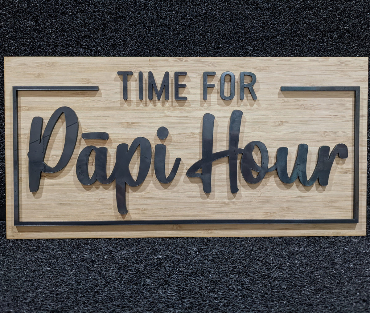 A rectangular wooden sign with the words 'TIME FOR Papi Hour' in raised dark lettering, displayed against a dark textured background.