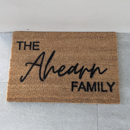 Personalised Doormat with 'The Family' text on a light gray floor.