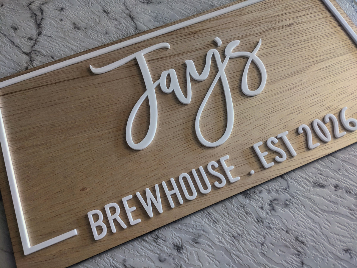 A personalized wooden sign with raised white lettering that reads "Jay's" and "BREWHOUSE . EST 2026," shown at an angle on a light stone surface.