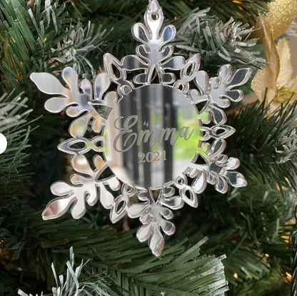 Silver snowflake ornament with 'Emma 2021' engraving on a Christmas tree.