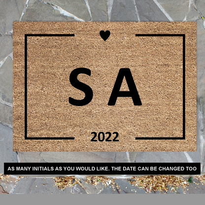 A customised rectangular coir doormat with black initials a small heart, and the year '2026