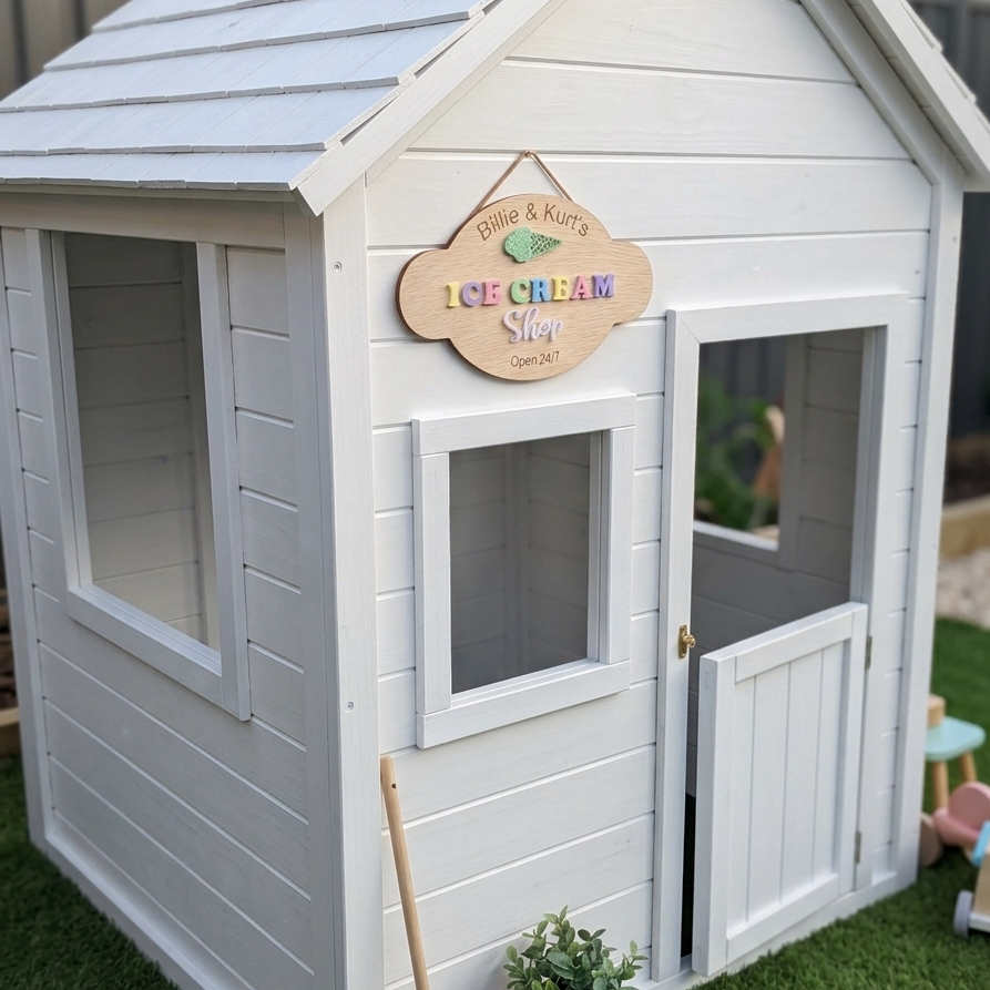Children's playhouse with 'Polly & K nuts Ice Cream Shop' sign on a grassy area.