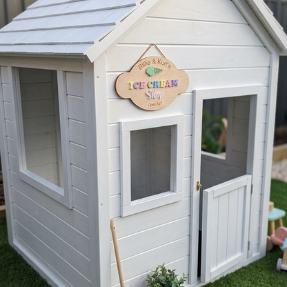 Children's playhouse with 'Polly & K nuts Ice Cream Shop' sign on a grassy area.