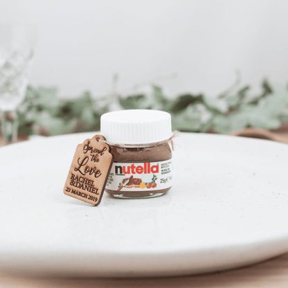 Small jar of Nutella with a personalized tag on a white surface with greenery in the background