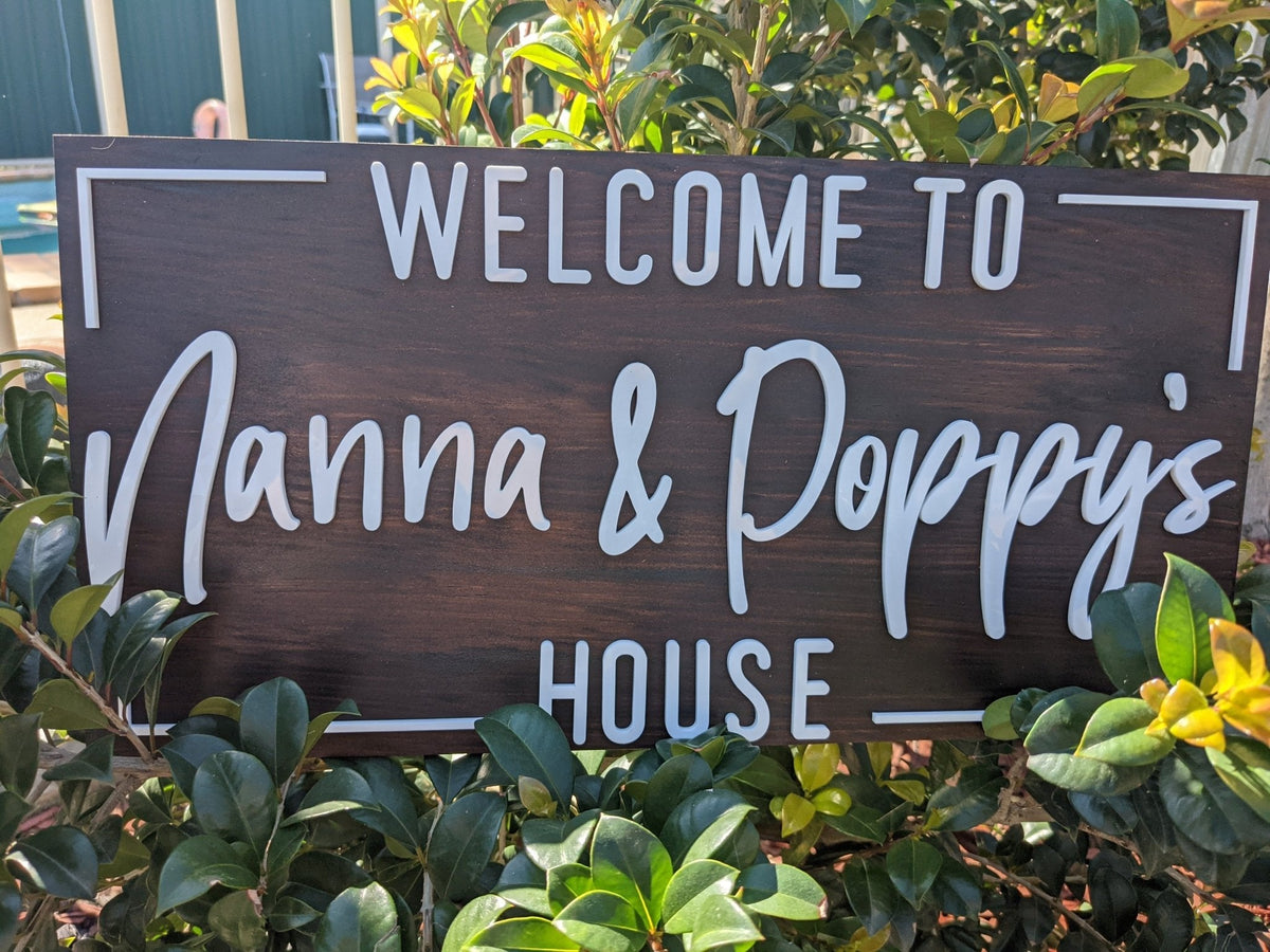 Wooden sign with 'Welcome to Nanna & Poppy's House' text, surrounded by greenery.