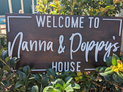 Wooden sign with 'Welcome to Nanna & Poppy's House' text, surrounded by greenery.