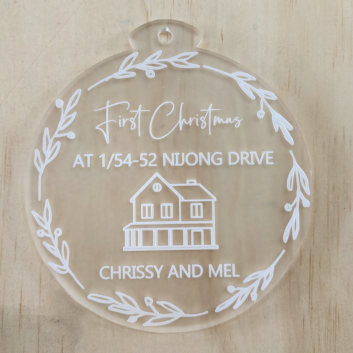 Decorative glass ornament with engraved text and house illustration on a wooden background