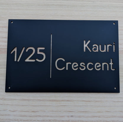 Black plaque with '1/25 Kauri Crescent' text on a wooden surface